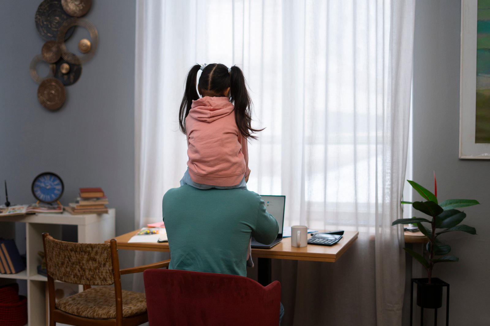 A parent struggles to focus on work with their child on their shoulders, representing the juggle of professional and family demands for busy parents.
