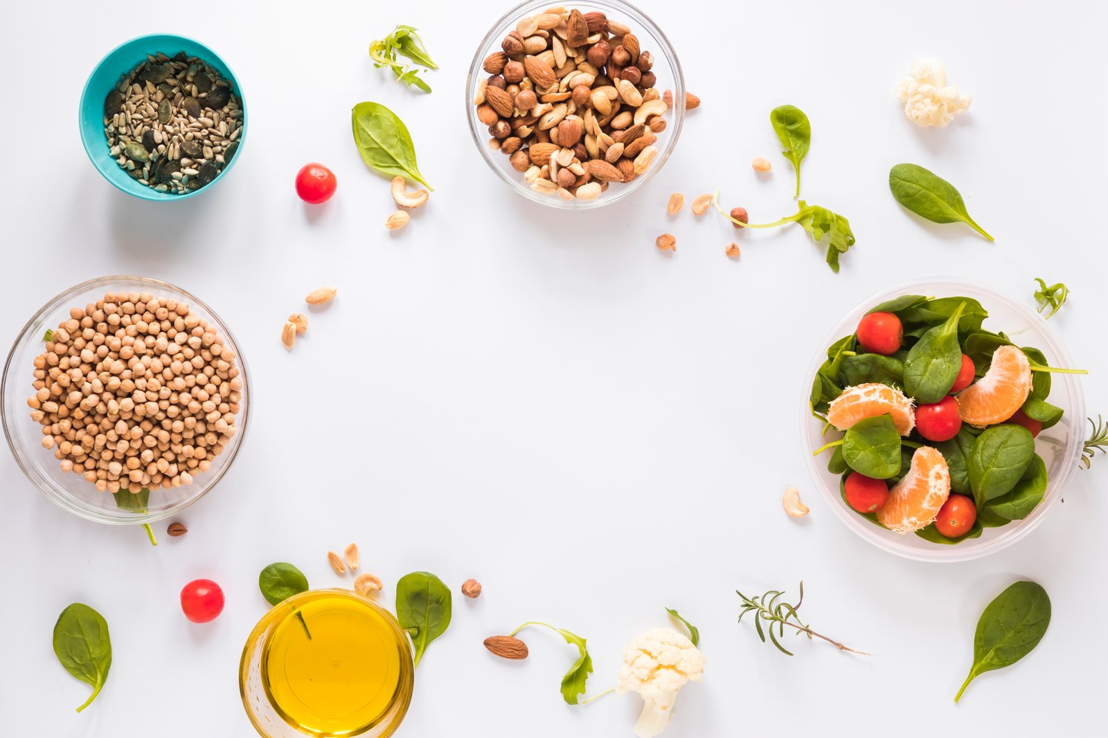 A flat lay of healthy, fresh ingredients including chickpeas, almonds, sunflower seeds, spinach, cherry tomatoes, tangerines, and olive oil, arranged on a white background with copy space in the center. Represents balanced and mindful eating through meal planning