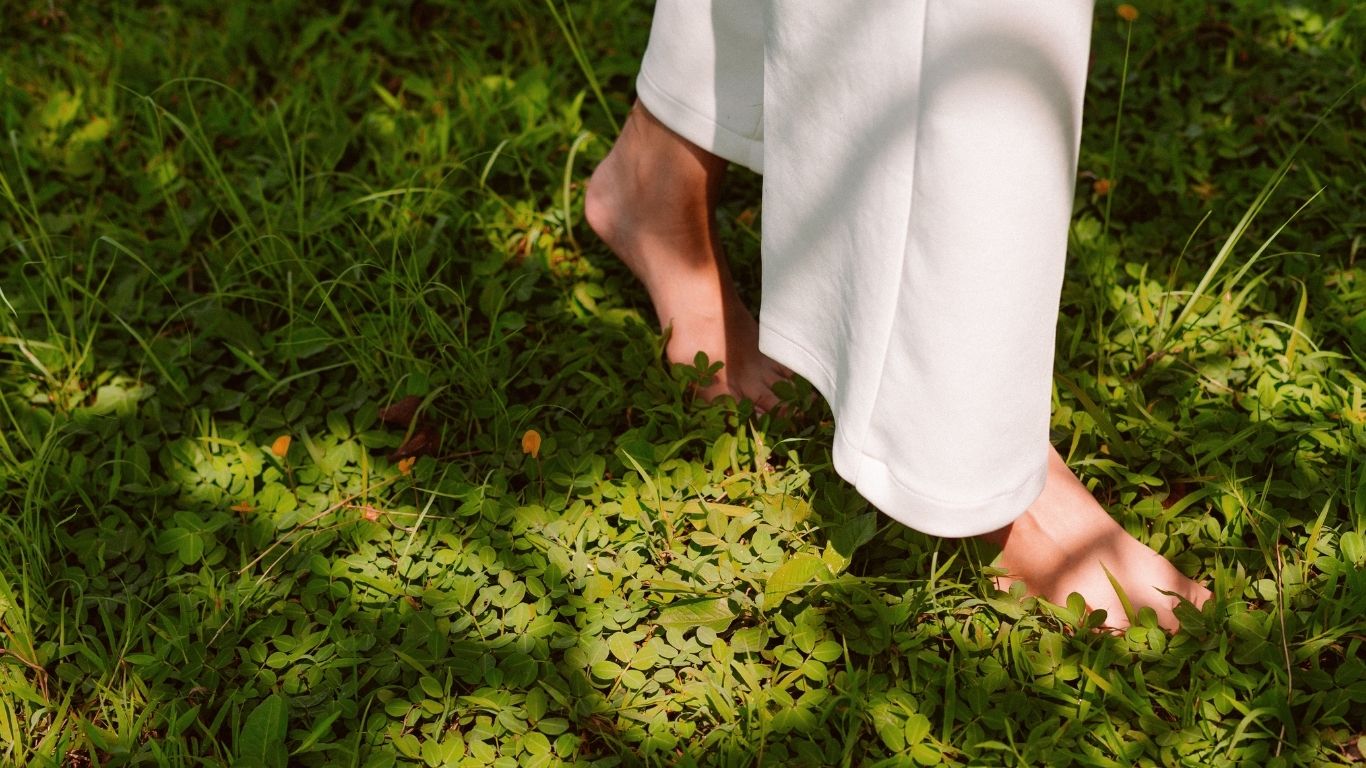 Bare feet walking on lush green grass in white pants